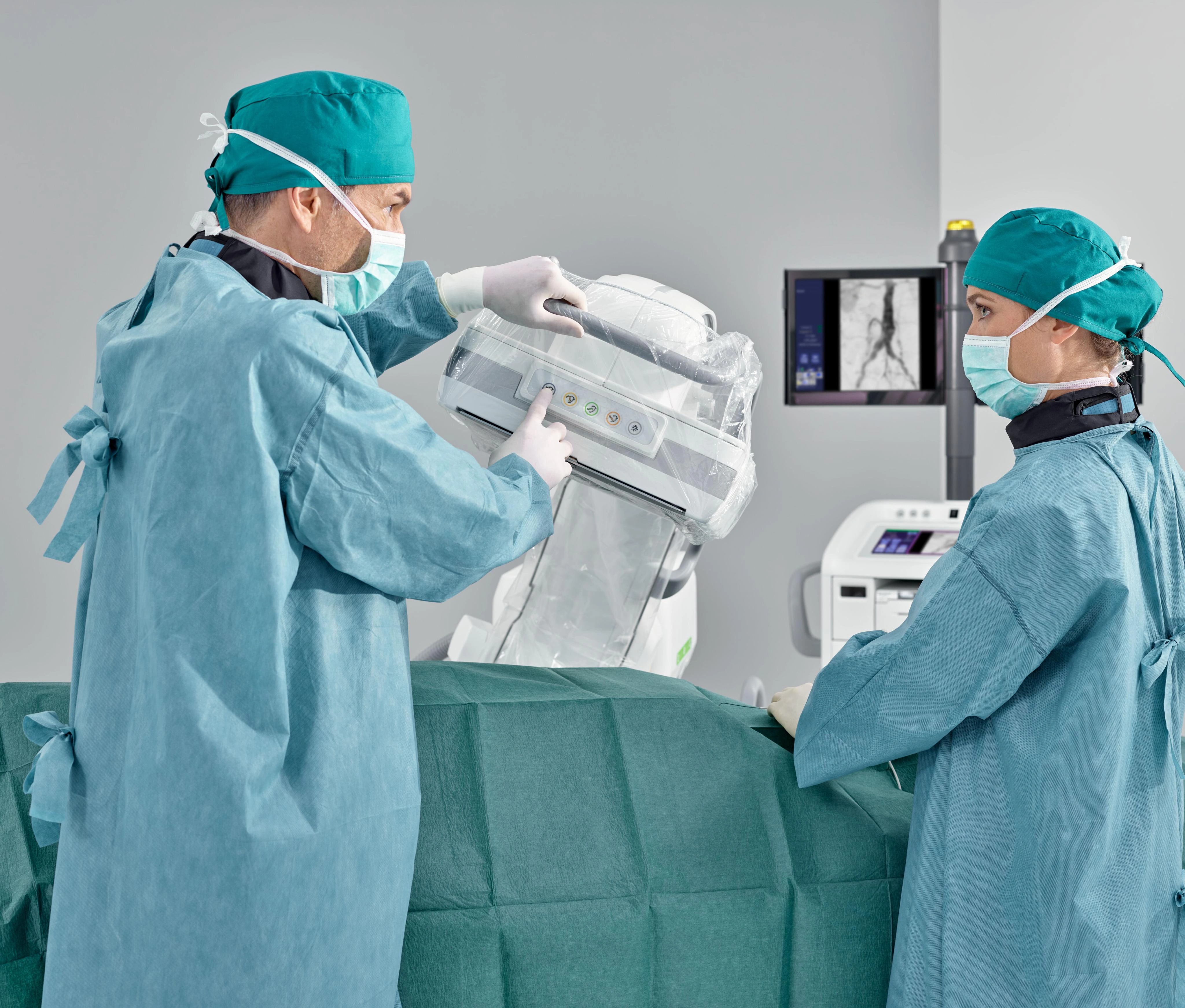 Profesionales sanitarios ajustan el detector enfundado del Cios Alpha junto a una mesa de procedimientos cubierta con paños, con imágenes visibles en el monitor.